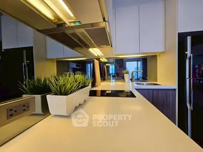 Modern kitchen with sleek countertops and built-in appliances, featuring stylish lighting and decorative plants.
