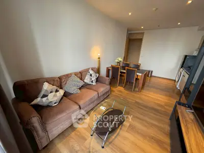 Modern living room with cozy sofa and dining area, featuring wooden flooring and ambient lighting.