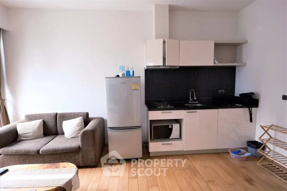 Modern studio apartment with compact kitchen and cozy living area, featuring wooden flooring and sleek appliances.