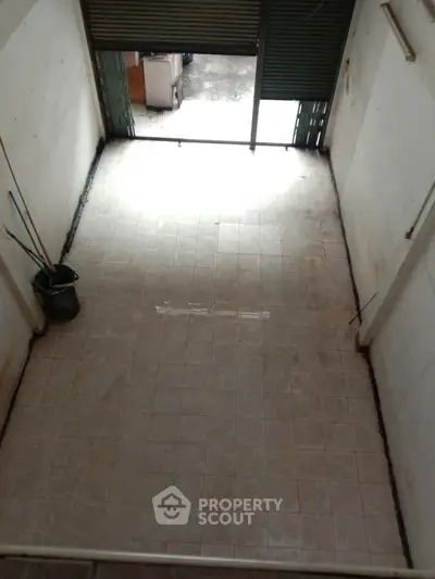 Spacious empty room with tiled floor and open shutter, ideal for storage or commercial use.