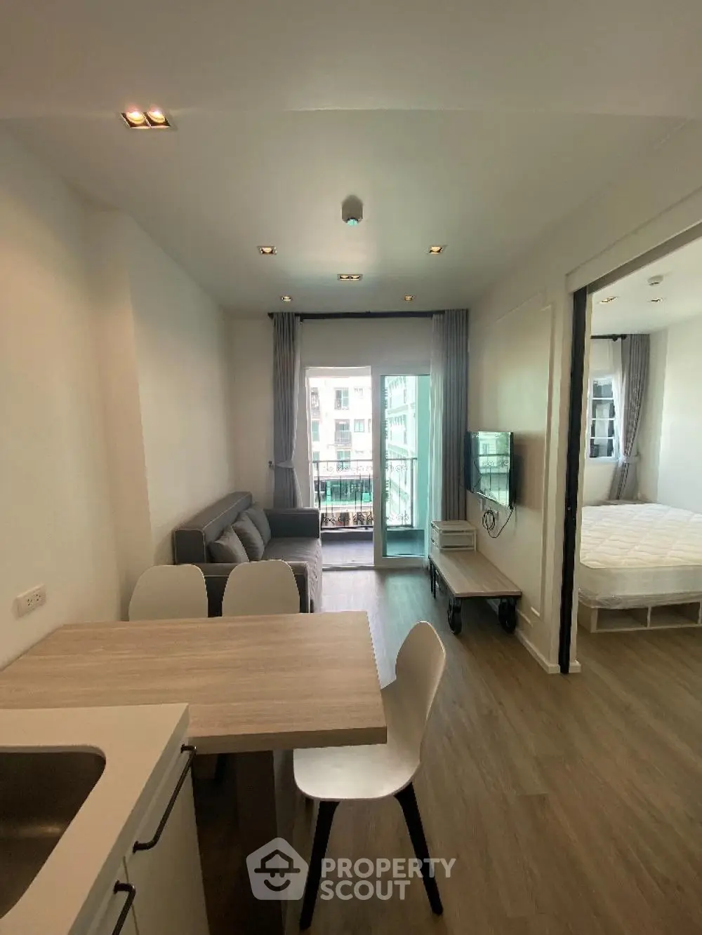 Spacious and well-lit studio apartment with modern furnishings, a cozy sleeping area, and a charming balcony with urban views.