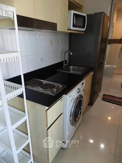 Compact kitchen with modern appliances and washing machine in a cozy apartment.