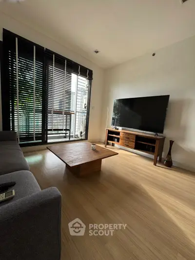 Modern living room with large TV and stylish wooden furniture, featuring floor-to-ceiling windows.
