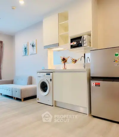 Modern studio apartment with compact kitchen and cozy living area, featuring washing machine and fridge.