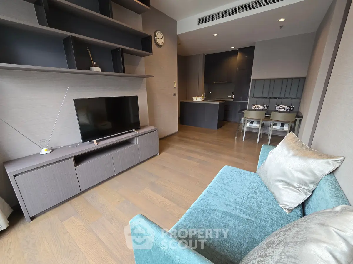 Modern living room with sleek furniture and open kitchen layout, featuring a stylish teal sofa and wall-mounted shelves.