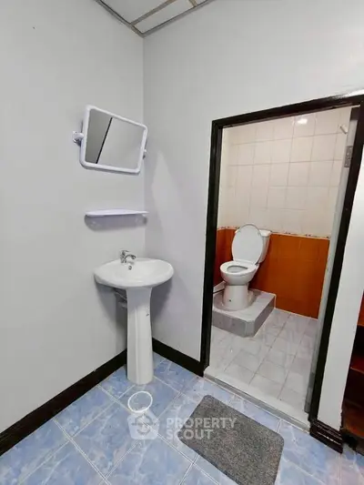 Compact bathroom with pedestal sink and toilet, featuring tiled flooring and a wall-mounted mirror.