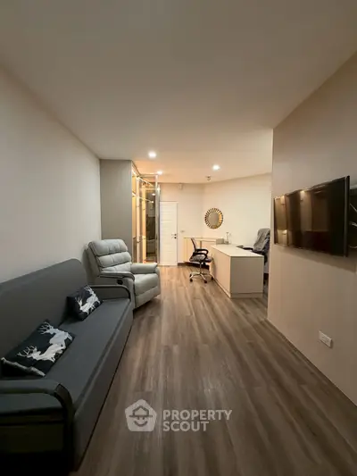 Modern living room with sleek furniture and wood flooring, featuring a wall-mounted TV and a cozy workspace.