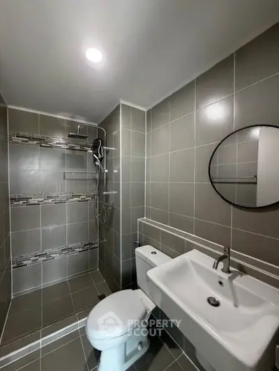 Modern bathroom with sleek tile design and round mirror, featuring a spacious shower area.