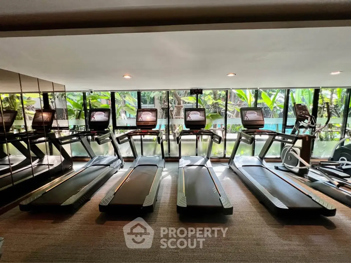 Modern gym with multiple treadmills and large windows overlooking greenery.