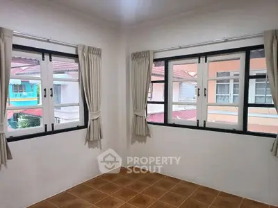 Bright corner room with large windows and tiled floor, offering a view of neighboring houses.