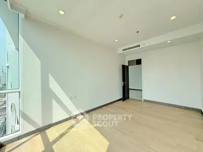 Spacious sunlit room with hardwood floors and large windows offering city views, perfect for modern living.