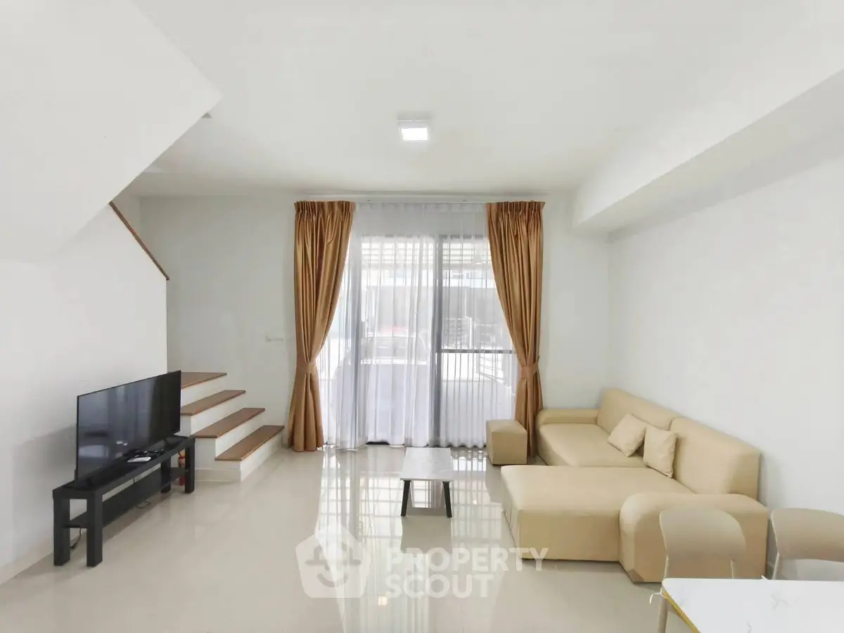 Spacious modern living room with beige sofa and TV, featuring elegant curtains and sleek staircase.