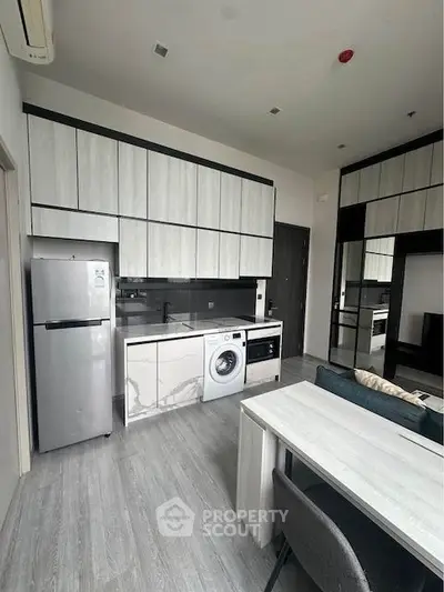 Modern kitchen with sleek cabinets, washing machine, and fridge in open layout.