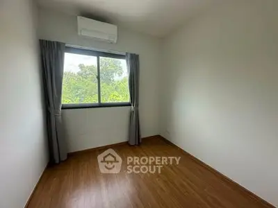 Bright empty bedroom with wooden flooring and large window overlooking greenery.