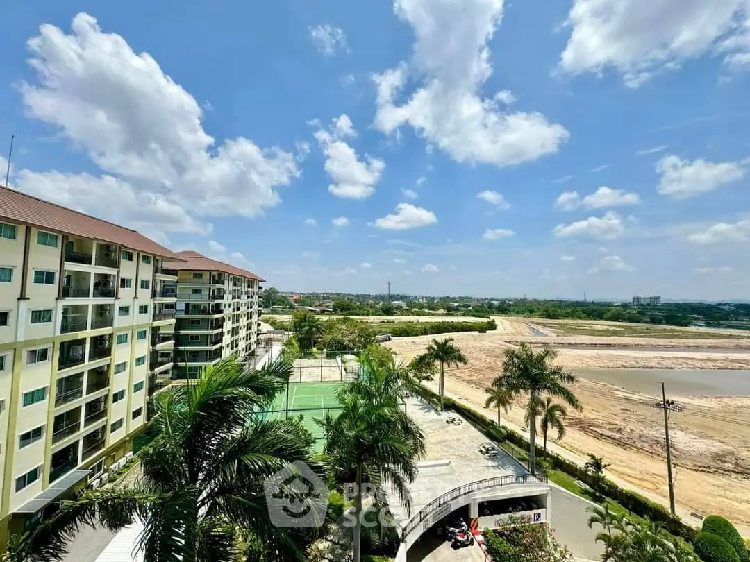 Stunning view of modern apartment complex with lush greenery and tennis court under a clear blue sky.
