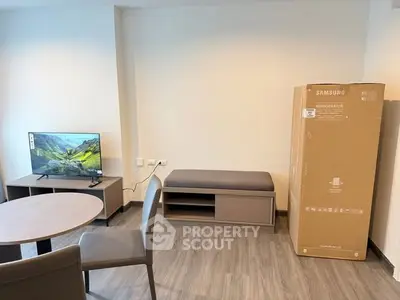 Modern living room with new Samsung refrigerator in box, stylish furniture, and flat-screen TV.