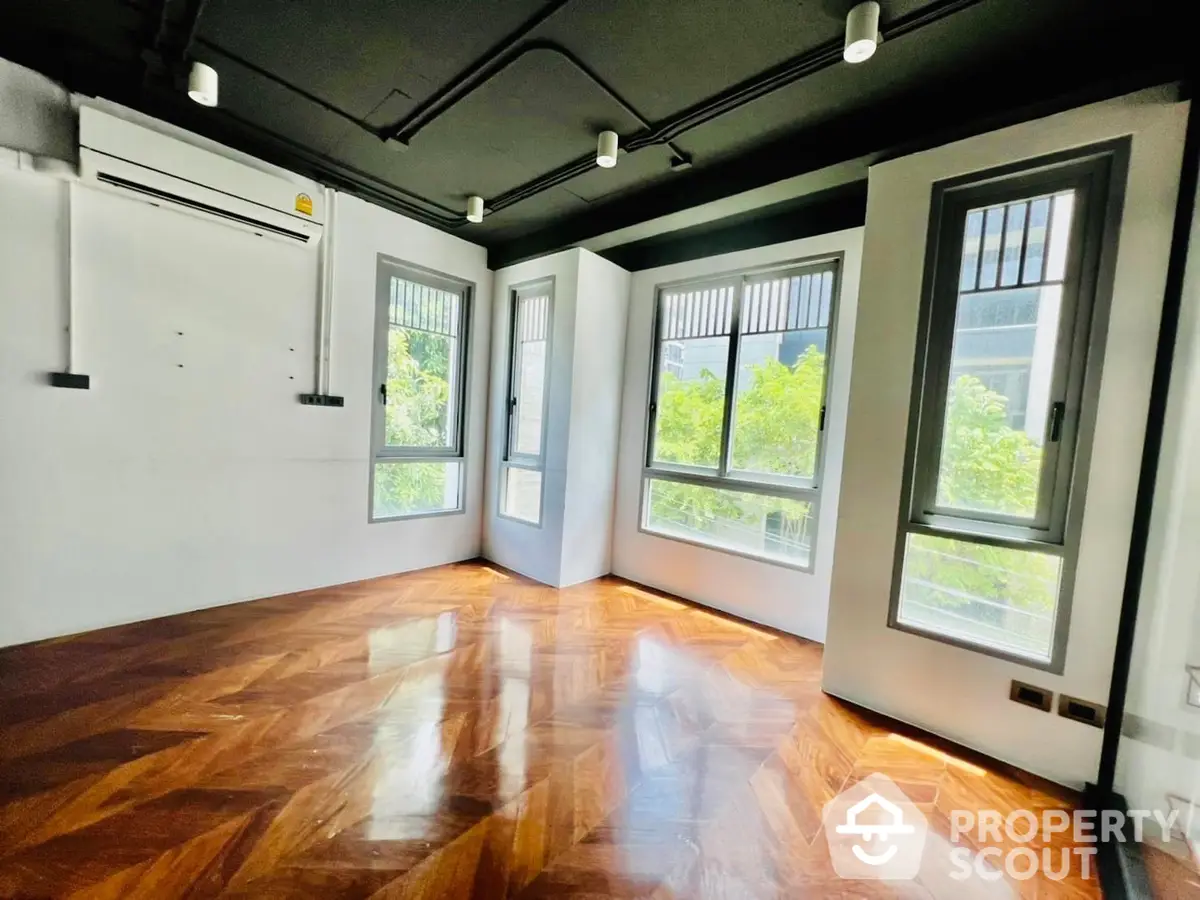 Spacious living room with polished hardwood floors, ample natural light, and a serene view of greenery through large windows, perfect for a modern lifestyle.