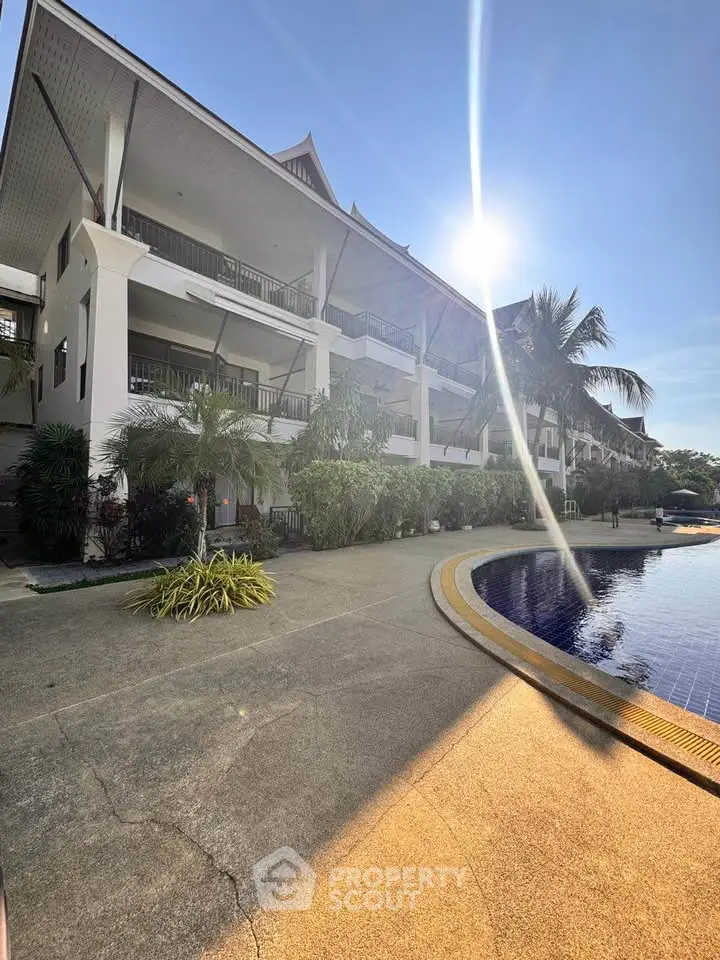 Stunning tropical resort with poolside view and lush greenery under a bright sunny sky.