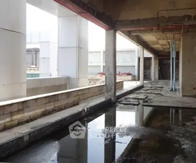 Spacious unfinished building with open layout and reflective water feature.