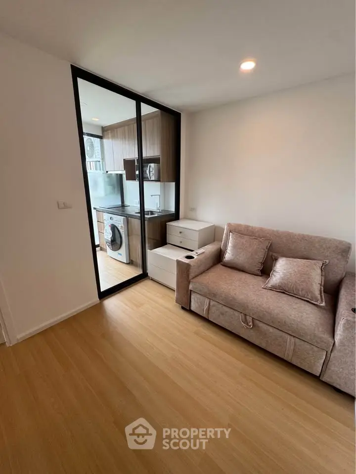 Modern living room with cozy sofa and open kitchen featuring washing machine and sleek cabinetry.