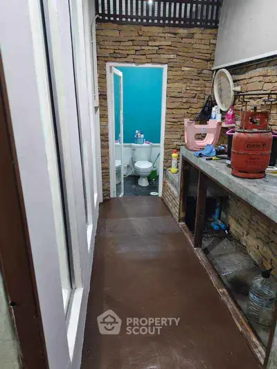 Unique narrow hallway leading to a small bathroom with rustic stone walls.