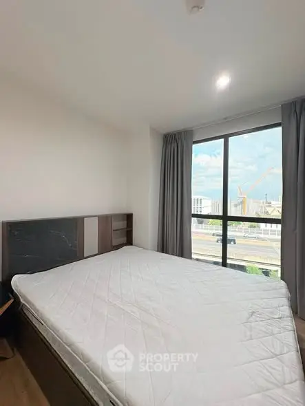 Spacious bedroom with large window offering city view, modern decor and ample natural light.