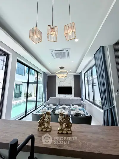 Luxurious modern living room with pool view, elegant dining setup, and stylish lighting fixtures.