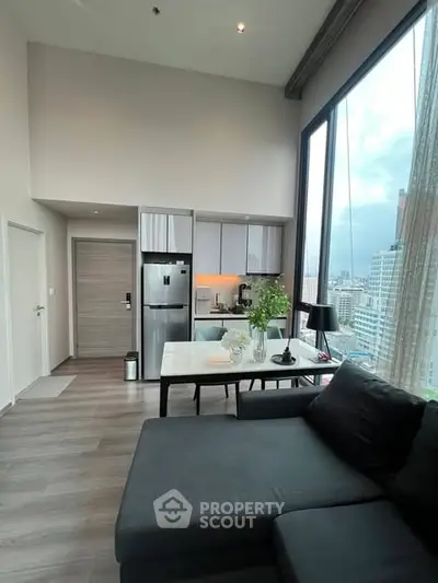 Modern living room with high ceiling and city view, featuring sleek kitchen and cozy seating area.