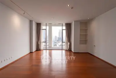 Spacious empty living room with wooden floors and large windows offering city views.