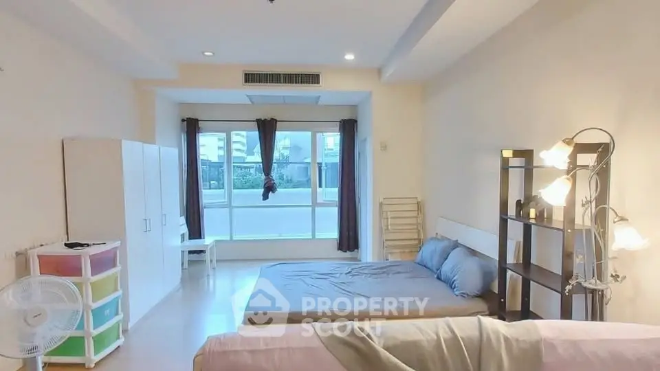 Spacious bedroom with large window and modern furnishings in a bright apartment.