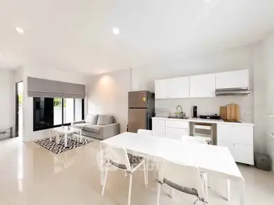 Spacious modern living room with open kitchen and dining area, featuring sleek white furniture and natural light.