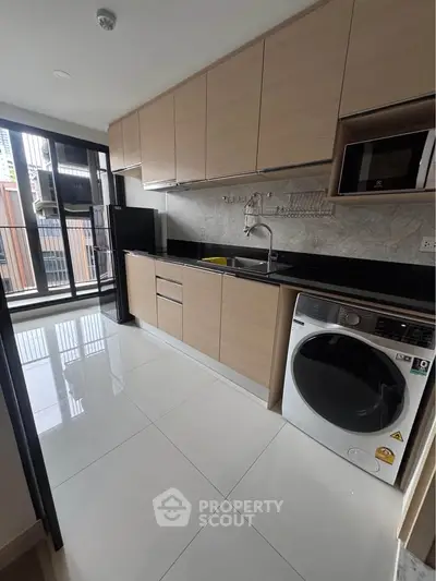Modern kitchen with sleek cabinetry, washing machine, and balcony access in a stylish apartment.