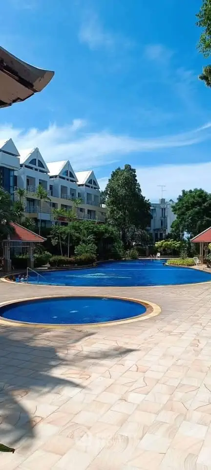 Stunning residential complex with a large pool and lush greenery under a clear blue sky.