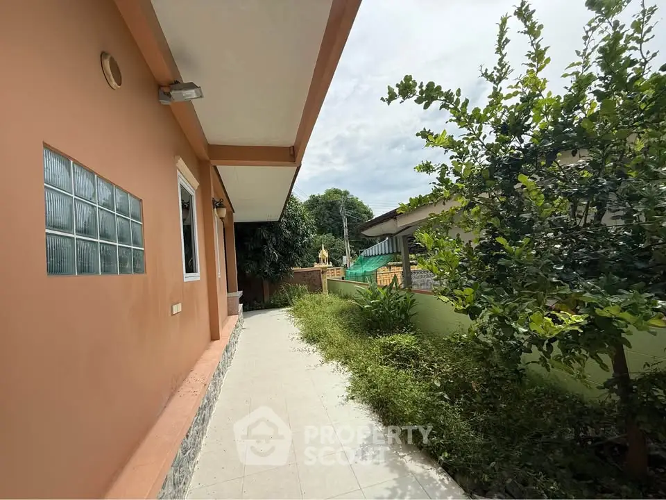 Charming exterior view of a single-story home with lush greenery and tiled pathway.
