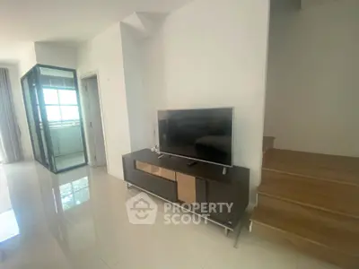 Modern living room with sleek TV stand and staircase, featuring glossy tiled floors and bright natural lighting.