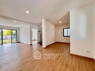 Spacious open-plan living room with wooden flooring and large windows for natural light.