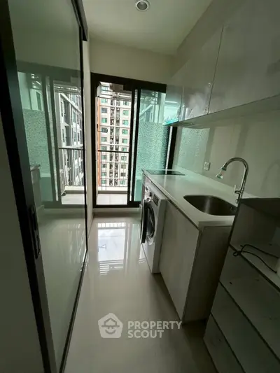 Modern compact kitchen with washing machine and balcony view in urban apartment.