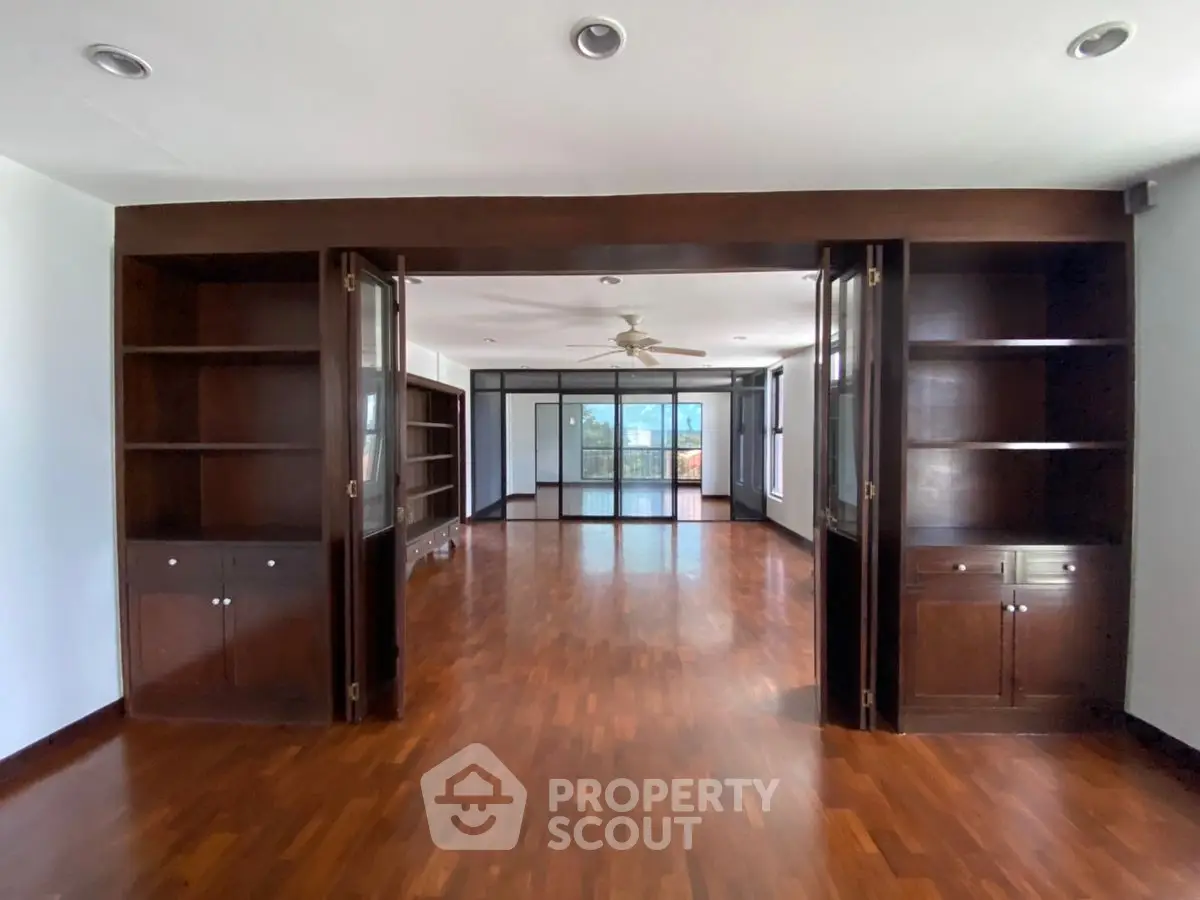 Spacious hardwood living room with built-in shelves and ceiling fan