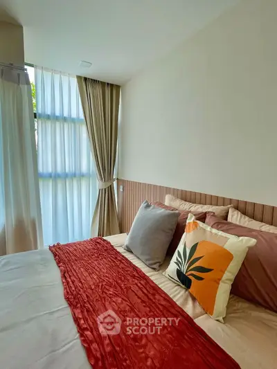 Cozy bedroom with stylish decor and natural light, featuring elegant curtains and vibrant pillows.