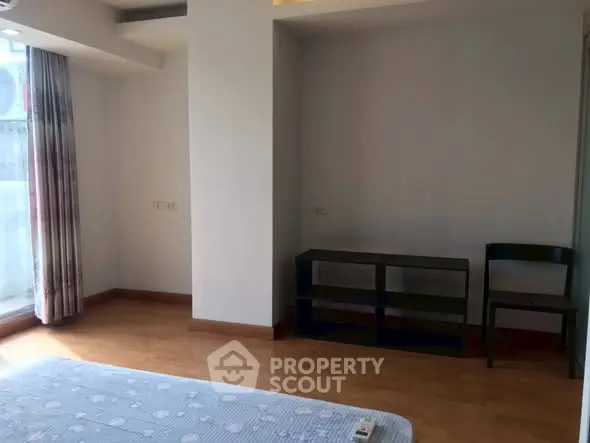 Spacious bedroom with wooden flooring and natural light