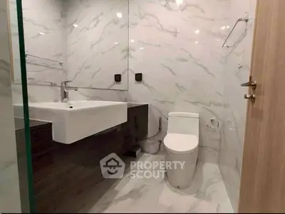 Modern bathroom with sleek design and marble tiles, featuring a stylish sink and toilet.