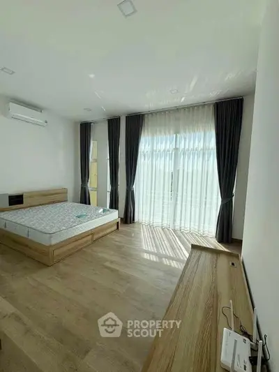 Spacious bedroom with large windows and natural light, featuring modern furnishings and elegant curtains.