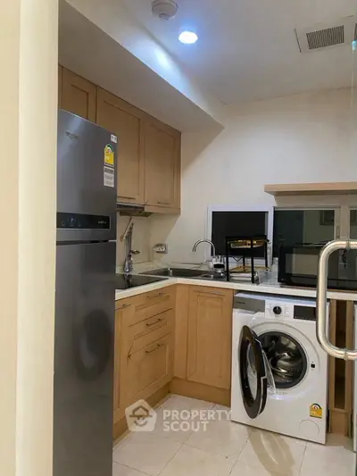 Modern kitchen with wooden cabinets, stainless steel fridge, and washing machine in cozy apartment.