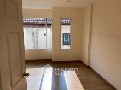 Bright empty room with wooden flooring and large windows in a residential property.