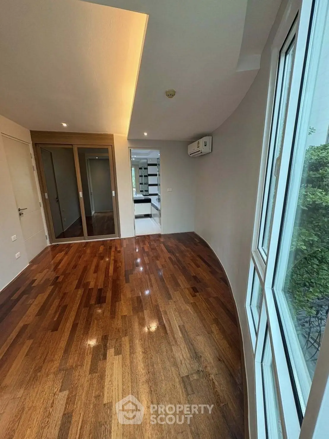 Spacious hardwood-floored room with large windows and modern design, perfect for stylish living.
