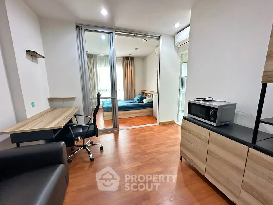 Modern studio apartment with wooden flooring, study desk, and cozy bedroom separated by glass doors.