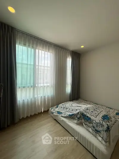 Cozy bedroom with large windows and elegant curtains, featuring a stylish bed and wooden flooring.