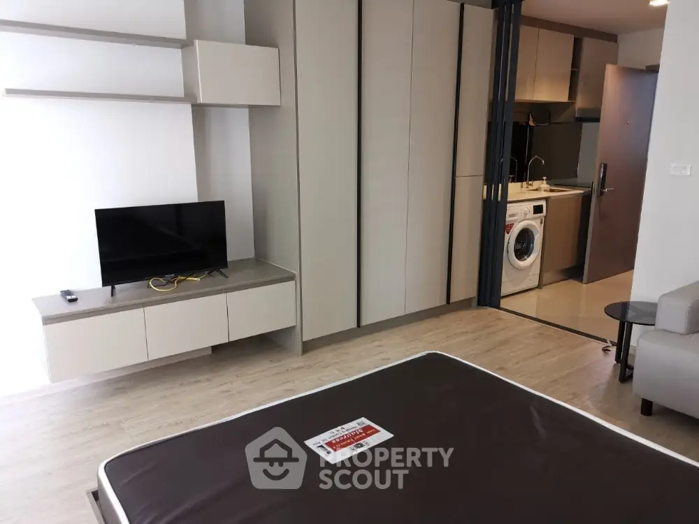 Modern studio apartment with integrated living space, featuring sleek built-in storage, a compact kitchen with appliances, and a cozy entertainment area.