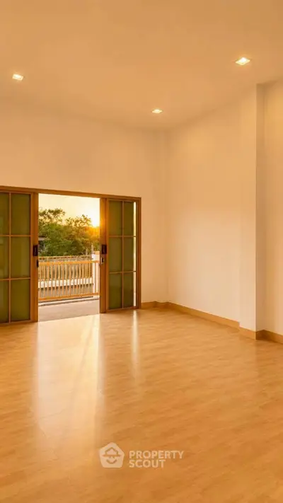 Spacious empty room with wooden flooring and sliding doors opening to a balcony with sunset view.