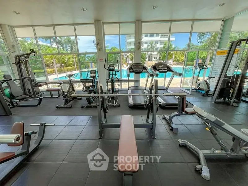 Spacious gym with modern equipment and pool view in luxury residential complex.